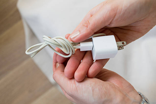 Woman sitting on floor unplugging and coiling a phone charging cable.