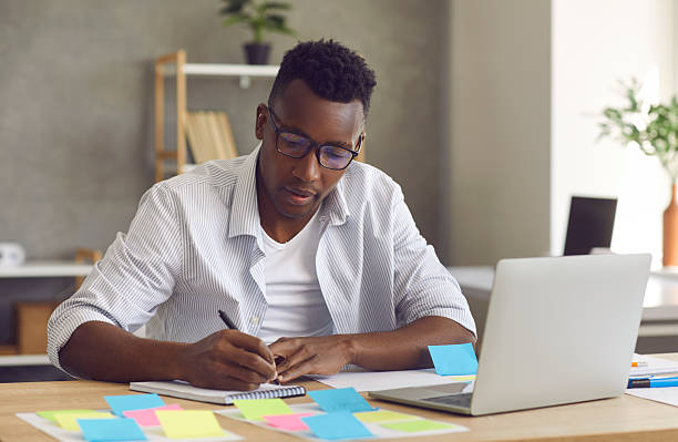 istock Young handsome minded black businessman writing down ideas in notebook 2214985864
