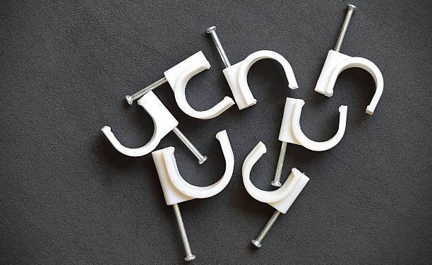 Table top view of scattered group of white color plastic or PVC material U shape clamp or saddle clips, used to hold wires cables or electrical tubes or pipes with metal nail flat lay over dark black background leather textured mat or slate or blackboard or road texture with copy space. Apt for construction or DIY home improvement posters, banners.