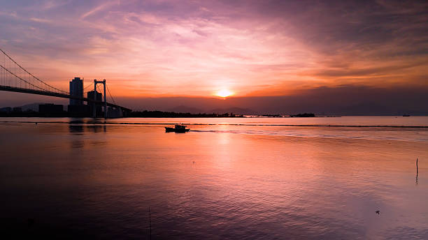istock Fishing boat gliding under cable stayed bridge, calm waters reflecting warm sunset hues, peaceful maritime landscape with serene atmospheric lighting 2214988719