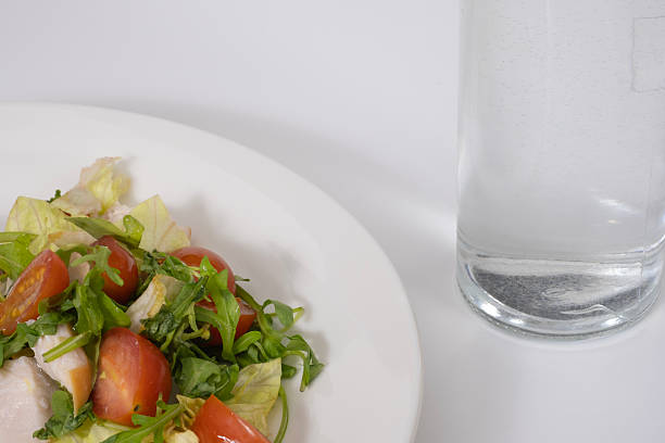 PlateA fresh and vibrant salad featuring lettuce, cherry tomatoes, and chicken pieces, paired with a glass of water. The clean white background enhances the healthy and minimalistic presentation, symbolizing wellness and balance