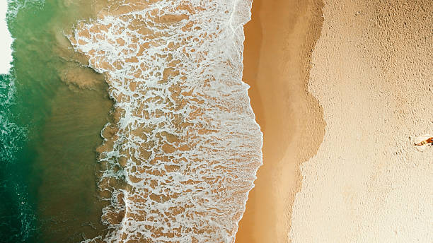 Aerial view revealing turquoise waves breaking over golden shoreline, highlighting dramatic color contrast between sparkling water and sunlit sandy beach
