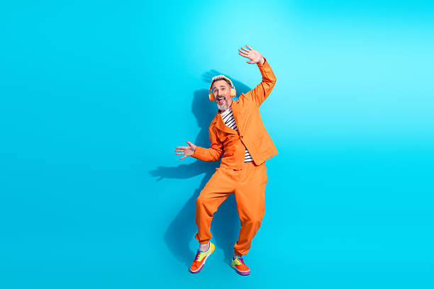 istock Energetic middle aged man in a vibrant orange suit joyfully posing with expressive gestures against a vivid blue background 2214994316