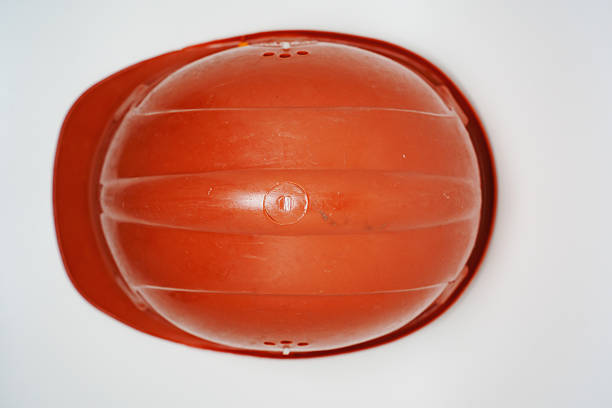 A bright orange safety helmet is positioned upside down on a plain white surface. It appears to be made of sturdy plastic and is commonly used in construction and industrial settings.