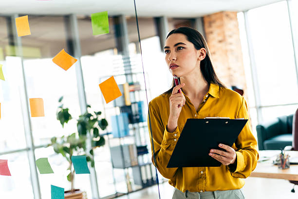 Thoughtful businesswoman analyzing tasks in a modern office environment with sticky notes. Professional attire and focused mind