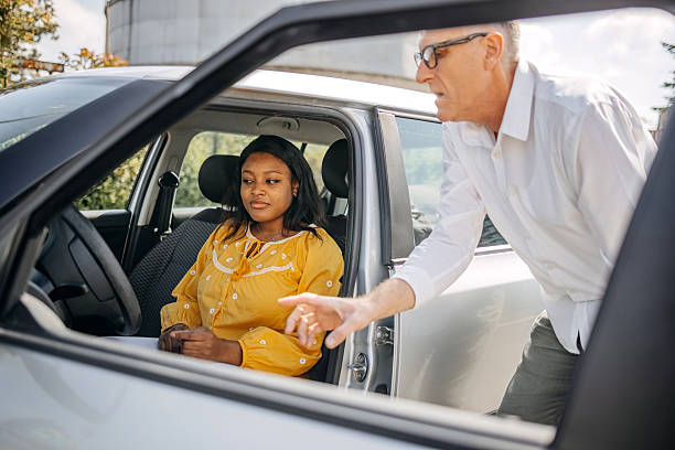 istock Young woman taking driving lessons with her instructor who is explaining driving basics 2215000755