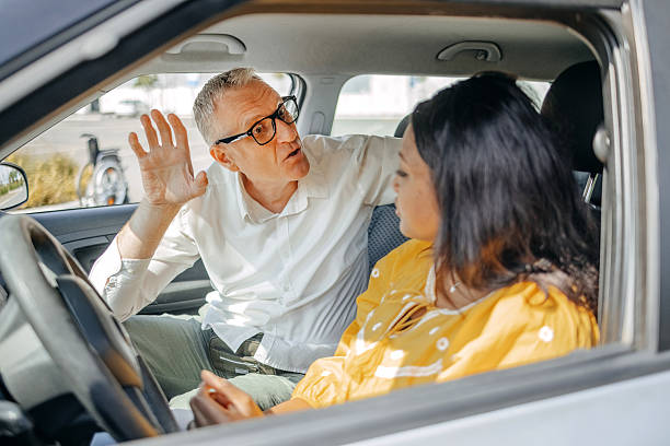 istock Young woman taking driving lessons with her instructor who is explaining driving basics 2215000939