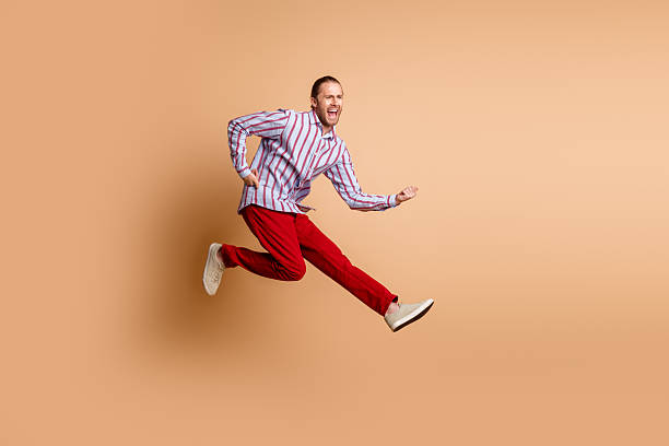 istock Energetic man in vibrant outfit jumping with joy on beige background showcasing dynamic energy and positivity for inspirational use 2215000972