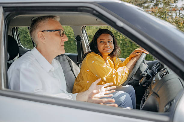istock Young woman taking driving lessons with her instructor who is explaining driving basics 2215000979