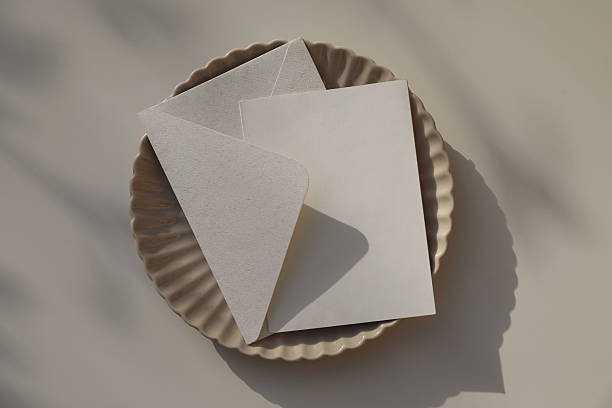 Beige fluted ceramic plate. Blank card, invitation mockup. Envelope in natural paper, softly lit by sunlight, shadows. Branding, birthday, wedding stationery. Elegant flat lay, neutral background.