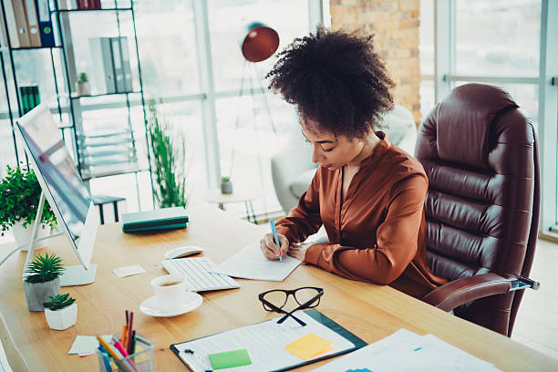 istock Businesswoman working at a bright office desk with computer and papers in a modern design loft style interior space 2215003192