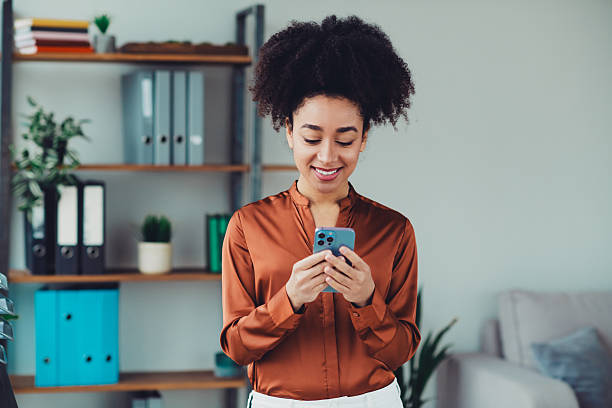 istock Confident young professional businesswoman browsing on her smartphone while standing in a stylish modern office with organized shelves 2215003308