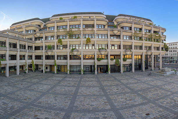 The city hall in Linz, Austria showcases a striking brutalist architecture with organic greenery incorporated into the design. The evening light reflects off the building's windows, creating a vibrant atmosphere in April 2025