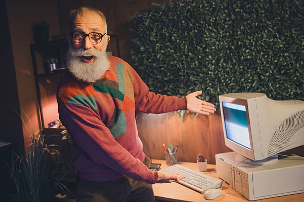 istock Elderly man proudly showing an old computer setup in a cozy home office with a vibrant sweater and a cheerful expression 2215004197