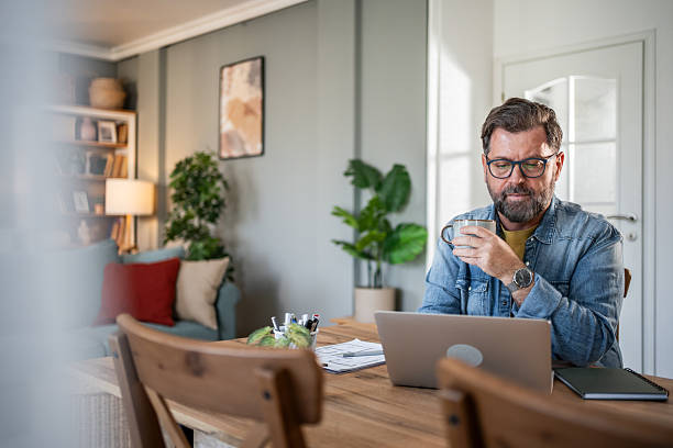 istock Focused middle aged freelancer drinking coffee and working on laptop at home 2215004844