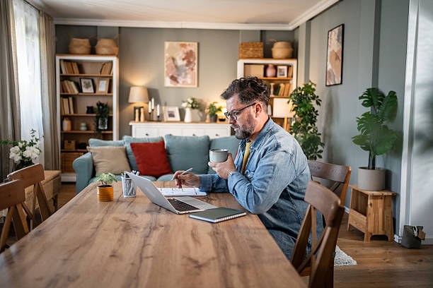 istock Focused mature man working from home, drinking coffee and using laptop 2215004865