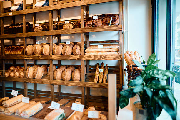 Freshly baked loaves of bread, baguettes, and sandwiches are neatly arranged on wooden shelves and display cases, creating an inviting atmosphere in a bakery shop