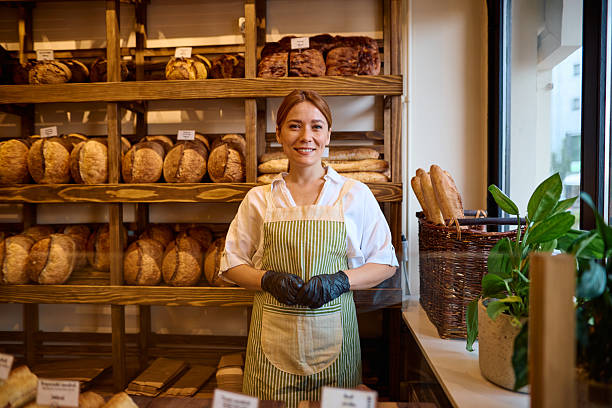 istock Female baker smiling wearing apron and gloves in bakery with bread display 2215007578
