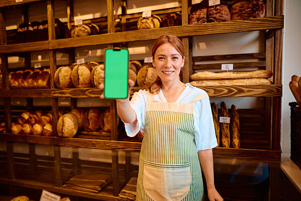 istock Smiling baker showing smartphone with green screen in bakery 2215008308