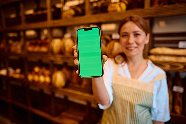 istock Smiling baker showing smartphone with green screen in bakery 2215008359