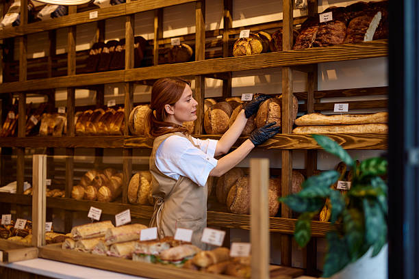 istock Baker arranging fresh bread on shelves in bakery shop 2215008488