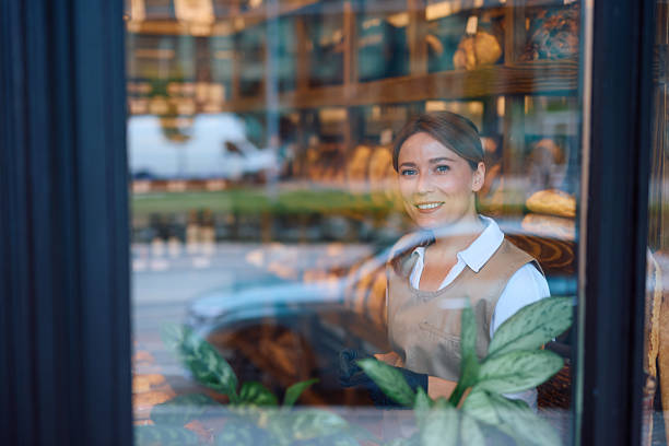 istock Smiling baker woman wearing black gloves looking at camera through bakery window 2215008803