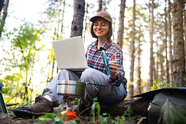 istock Young woman camping in forest using a laptop with cooking equipment 2215009782