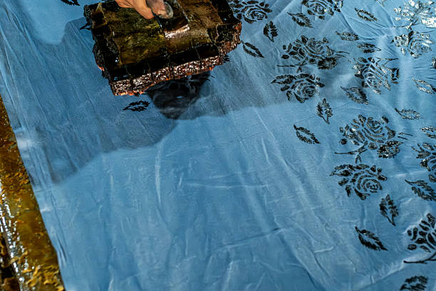 Hand printing a vibrant floral design onto blue fabric using a traditional batik stamp, showcasing intricate craftsmanship and cultural heritage