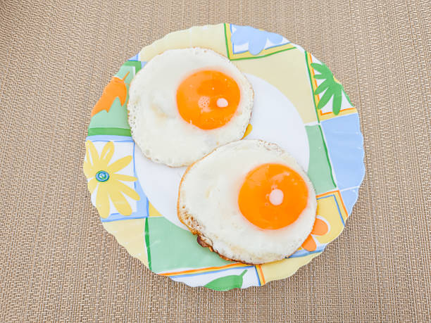 Two perfectly fried eggs are served on a vibrant, floral patterned plate, creating a simple yet appealing breakfast presentation
