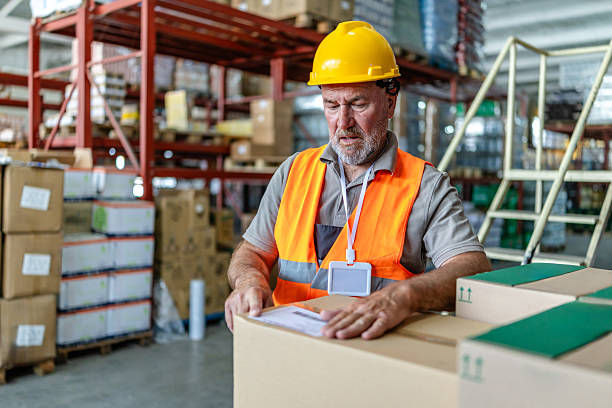 istock Warehouse worker examining boxes and paperwork while wearing safety gear in a distribution center 2215017246