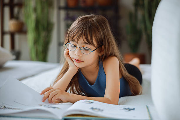 istock Beautiful little girl reading book lying on the sofa. 2215017980