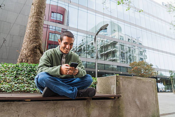 Happy young adult using his phone in a city park, enjoying social media and mobile technology