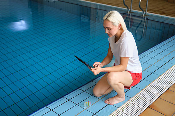 istock Pool maintenance worker checking water quality on a tablet next to test tubes 2215021292