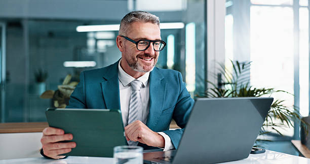 maturo, uomo d'affari e tablet con computer portatile in ufficio, rapporto finanziario e revisione contabile per società aziendale. carriera, uomo e contabile con tecnologia per la ricerca sugli investimenti, l'amministrazione e il sorriso - businessman foto e immagini stock