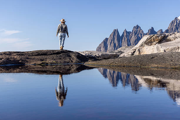 Individual in casual attire stands by a reflective lake, taking in snow-capped mountains. Scenic landscapes with clear skies. Travel, nature exploration, serenity.