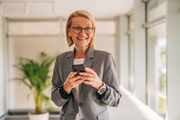 istock Smiling senior businesswoman using smartphone in office hallway 2215029814