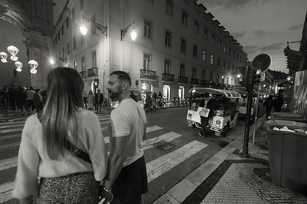 Lisbon, Portugal - November 30, 2024: A tuk-tuk driver waits for clients by his tuk-tuk while holding a menu card at a street in Lisbon downtown.