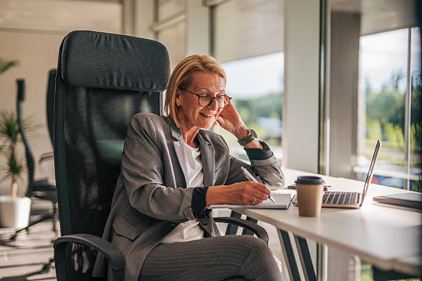 istock Senior businesswoman taking notes while working on laptop in office 2215031939