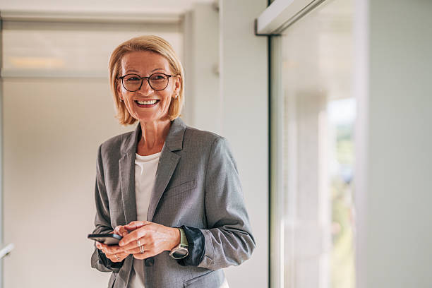 istock Smiling senior businesswoman using smartphone in office corridor 2215032358