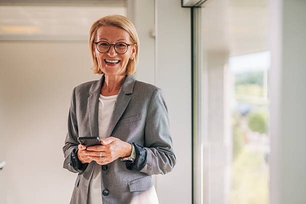 istock Smiling senior businesswoman using smartphone in office corridor 2215032361
