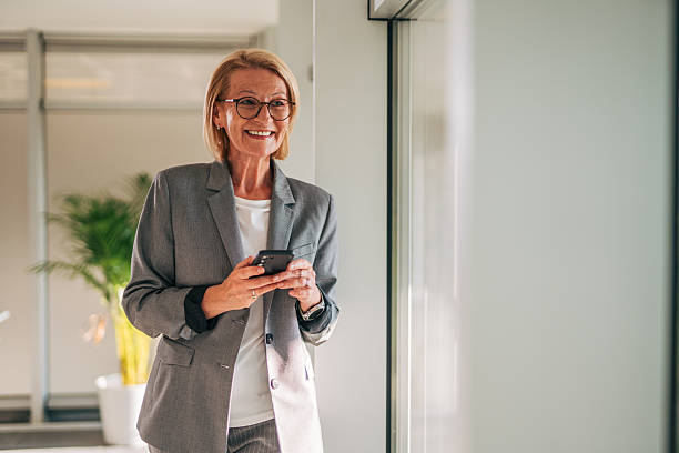 istock Smiling senior businesswoman using smartphone in office corridor 2215032496