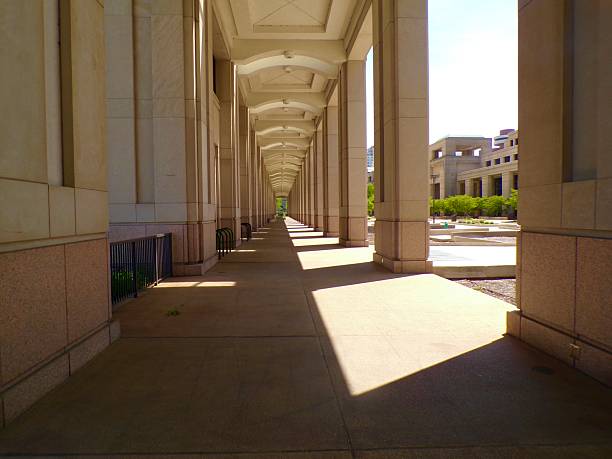 A walkway formed by concrete columns decorated with horizontal stripes unfolds in a dynamic motion blur, evoking a sense of contemporary design and movement. A red car zooms past on the adjacent street.