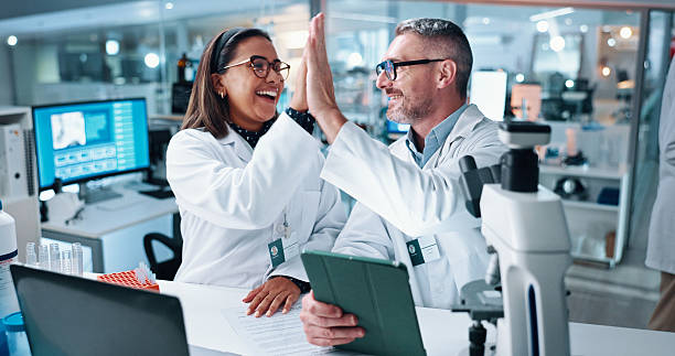 istock High five, science and tablet with people in laboratory together for breakthrough or development. Laptop, microscope and success with research team in clinical trial for celebration, goals or target 2215035695