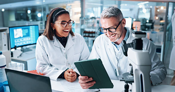 istock Funny, science and tablet with people in laboratory together for breakthrough or development. Comedy, laptop and microscope with happy research team joking or laughing at results of clinical trial 2215035697