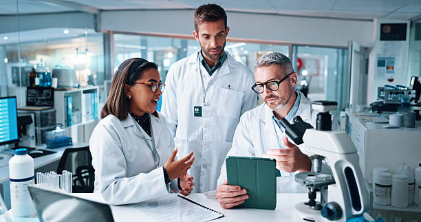 istock Discussion, science and tablet with people in laboratory together for breakthrough or development. Conversation, laptop and microscope with professional research team in clinical trial for discovery 2215035698