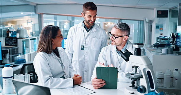 istock Science, tablet and talking with people in laboratory together for breakthrough or development. Collaboration, laptop and microscope with medical research team in clinical trial for discussion 2215035699