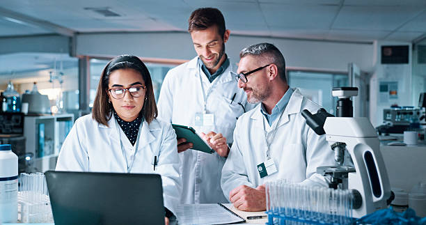 istock Laptop, science and tablet with people in medical lab together for breakthrough or development. Collaboration, computer or microscope with mentor and research team in clinical trial for discovery 2215035714
