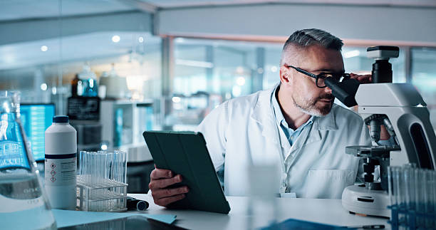 istock Scientist, mature man and microscope with tablet, study and medical research for human genome sequence. Person, touchscreen and clinical trial with application, reading and DNA analysis in laboratory 2215035725