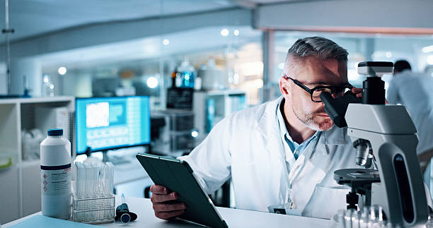 istock Scientist, man and microscope with tablet, analysis and medical research for human genome sequence. Mature person, touchscreen and clinical trial with app, investigation and DNA study in laboratory 2215035735