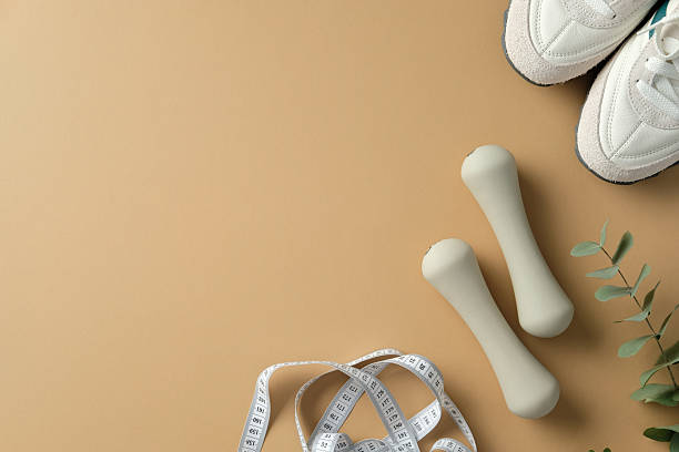 istock Sport equipment: dumbbells, measuring tape, and sneakers on a beige backdrop 2215037428